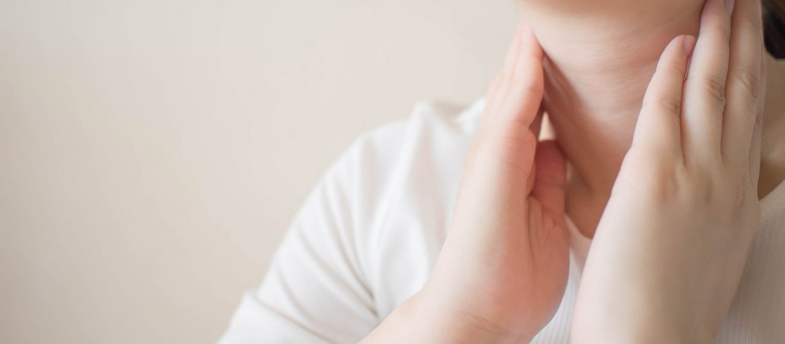 Female checking thyroid gland by herself. Close up of woman in white t- shirt touching neck. Thyroid disorder includes goiter, hyperthyroid, hypothyroid, tumor or cancer. Health care. Copy space.