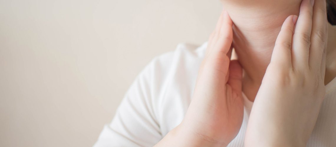 Female checking thyroid gland by herself. Close up of woman in white t- shirt touching neck. Thyroid disorder includes goiter, hyperthyroid, hypothyroid, tumor or cancer. Health care. Copy space.